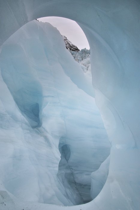 Ice cave in a glacier in New Zealand. Layers of the glacier are visible in some of the walls of the cave.
