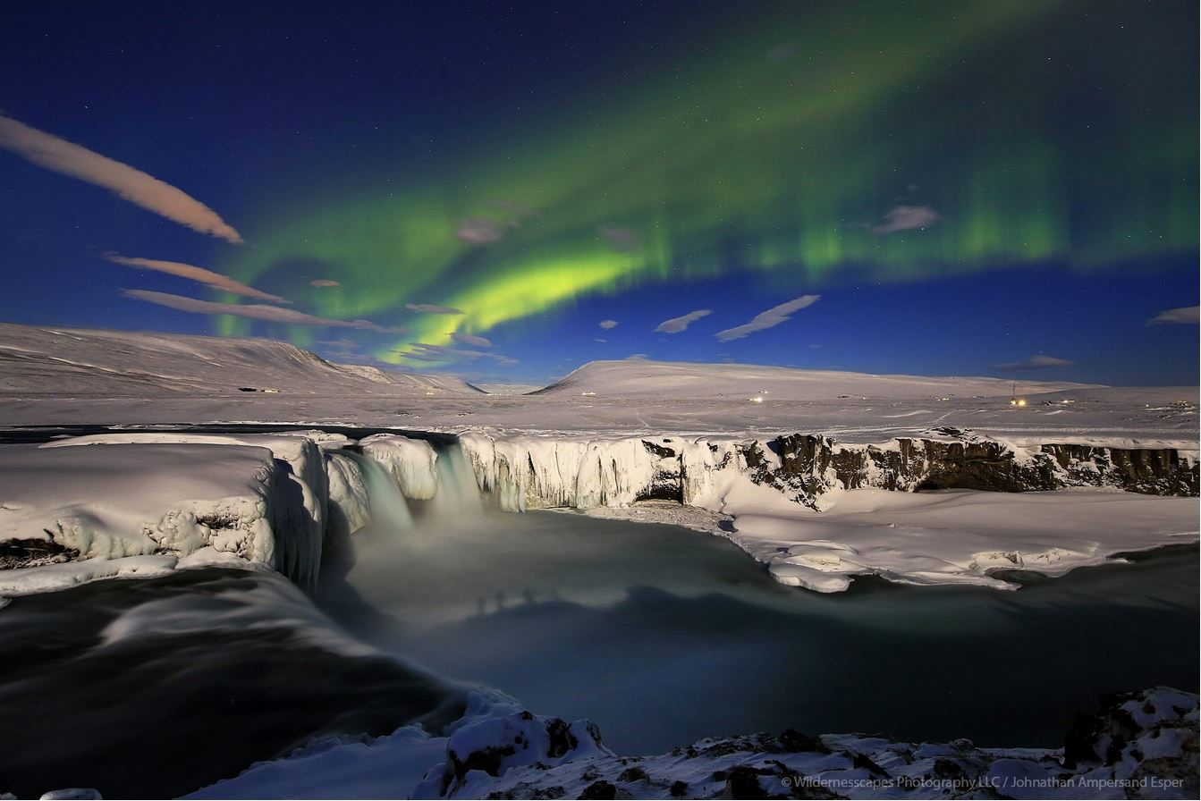 Full moon Auroras over Go&eth;afoss Waterfall, Iceland. Photographers sillouettes in the full moon can be seen in the water.