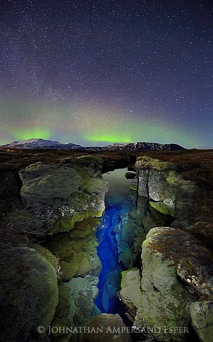 Aurora borealis display over Silfra tectonic plate crack, &THORN;ingvellir National Park, Iceland, natural color of water with...